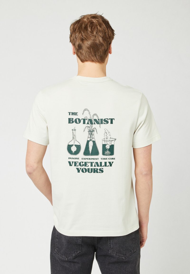 Crème-kleurig katoenen t-shirt met groene tekst en botanische grafische ontwerpen op de achterkant, met een ontspannen pasvorm en korte mouwen.