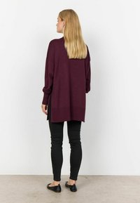 Burgundy long-sleeve sweater with a relaxed fit, side slits, and ribbed hem, paired with black slim-fit jeans and black flats.