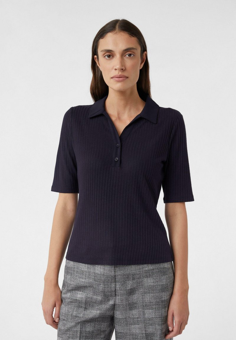 Granatowa koszulka polo z prążkowanego materiału, z krótkimi rękawami, zapięciem na trzy guziki i płaskim kołnierzykiem. W połączeniu z szarymi spodniami w teksturowany wzór w kratę.