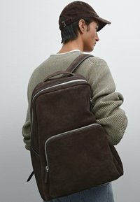 Brauner Wildleder-Rucksack mit glatter Textur, ausgestattet mit einem großen Hauptfach, einer vorderen Reißverschlusstasche und verstellbaren Schulterträgern.