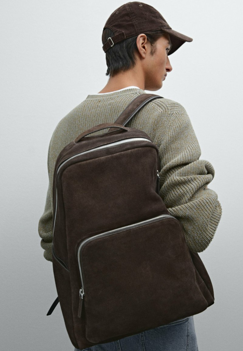 Brauner Wildleder-Rucksack mit glatter Textur, ausgestattet mit einem großen Hauptfach, einer vorderen Reißverschlusstasche und verstellbaren Schulterträgern.