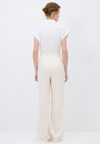 Blouse blanche à manches courtes avec un col, associée à un pantalon large à rayures beige clair avec une coupe ajustée et des poches arrière.