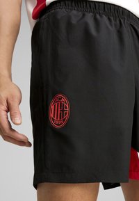 Čierne športové šortky s elastickým pásom. Na prednej strane sa nachádza červené kruhové logo s nápismi "ACM" a "1899". Vyrobené z hladkého, ľahkého materiálu.