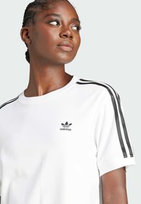 Vit bomull t-shirt med svart Adidas-logotyp på bröstet. Har svarta ränder längs axlarna och en klassisk rund halsringning.