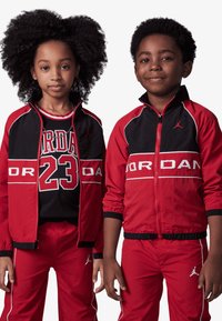 Rote und schwarze sportliche Jacken mit weißen Akzenten, versehen mit "JORDAN"-Markenlogo. Die linke Jacke hat einen Mesh-Oberteil mit der Zahl "23" und einem gestreiften Kragen.