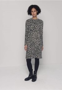 Dlouhé šaty s leopardím potiskem v odstínech šedé a černé, doplněné černými legínami a kotníkovými botami. Měkká látka s volným střihem.