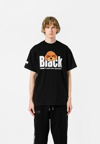 Camiseta de algodón negra con un gráfico de un perro de peluche en naranja y marrón, con el texto en blanco "Black" en negrita y un texto más pequeño debajo.