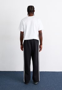 White short-sleeve t-shirt and black sweatpants with white side stripes, shown from the back on a blue carpet.