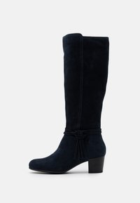 Marina mockasknäliga stövlar med rund tå, blockklack och en knytning vid vristen. Slät textur och minimala sömdetaljer.