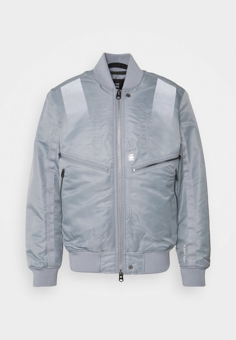 Veste bomber gris clair avec col, poignets et bas côtelés, fermeture éclair devant, deux poches zippées horizontales et patchs réfléchissants blancs aux épaules.