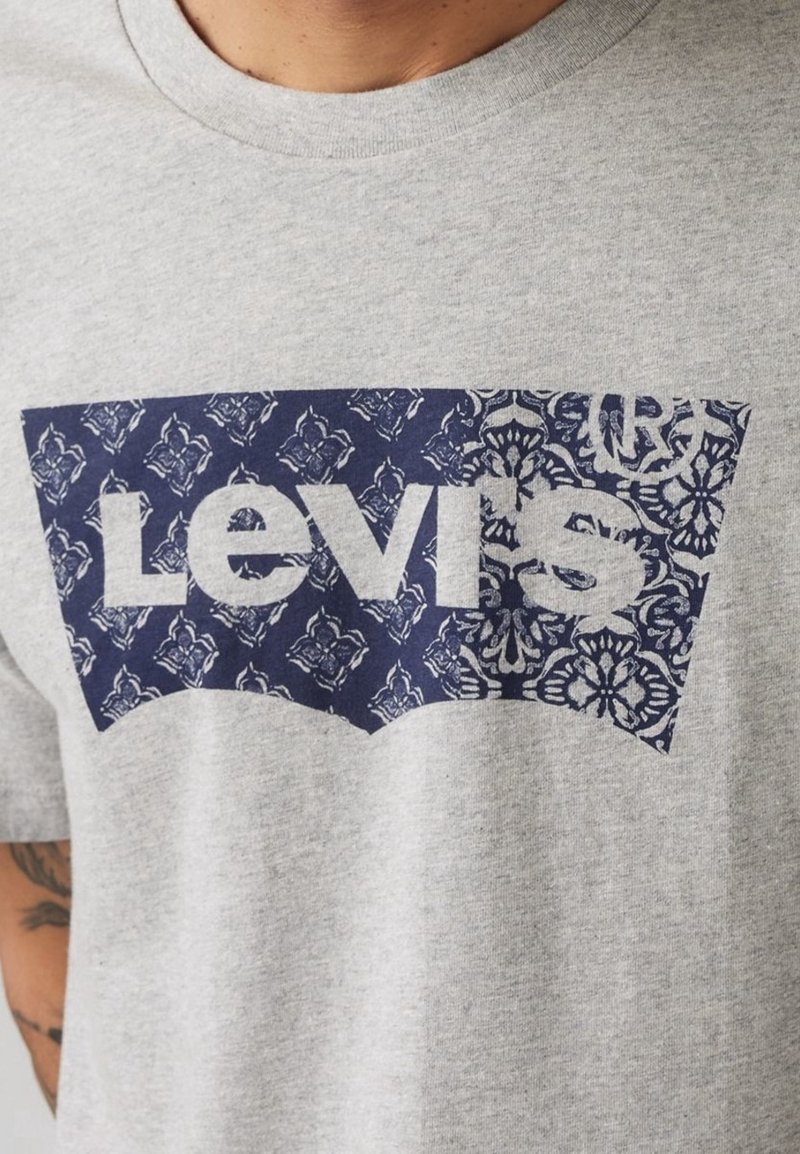 T-shirt en coton gris arborant un grand logo Levi's bleu avec un motif floral. Design classique à col rond, manches courtes.