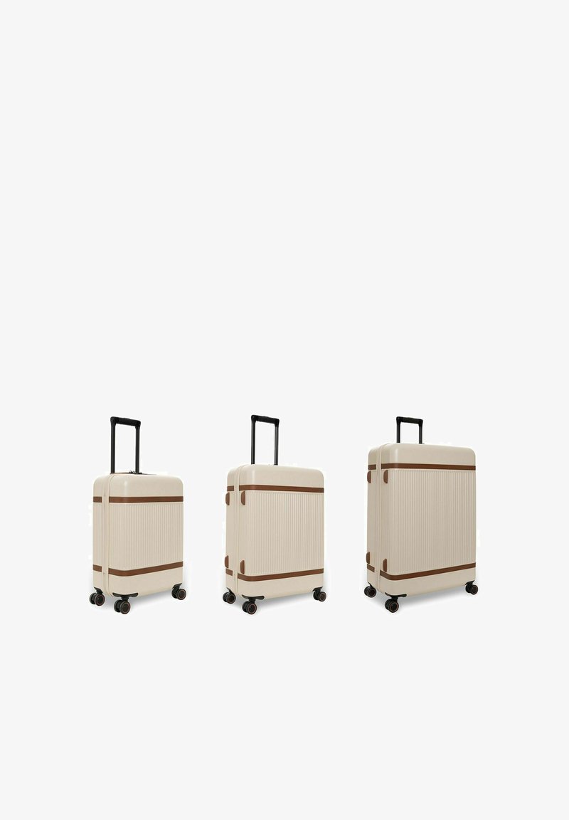 Trois valises rigides couleur crème avec des sangles marron et des poignées téléscopiques noires, présentées côte à côte en petites, moyennes et grandes tailles.