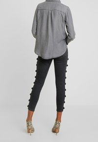 Camicia in denim grigio con plissettature sul retro, abbinata a jeans skinny scuri con dettagli in pom-pom lungo il lato e tacchi a spillo in stampa serpente.