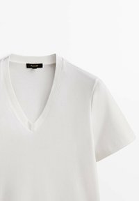 T-shirt blanc à manches courtes avec col en V et une étiquette noire à l'intérieur du col à l'arrière, présenté sur un fond blanc.