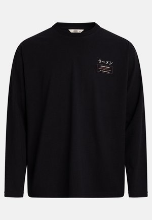 Črna majica z dolgimi rokavi in okroglim izrezom, z majhnim belim in oranžnim napisom na levi strani prsnega koša, ki vključuje japonske znake in znak "Delovni čas".