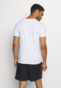 White short-sleeve t-shirt made of cotton, round neckline, smooth texture, paired with black athletic shorts, showing a back view.