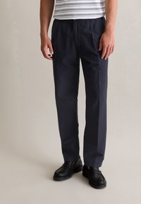 Marineblauwe, lichte broek met elastische taille en een ontspannen pasvorm. Geaccentueerd met subtiele textuur en gecombineerd met zwarte instappers.