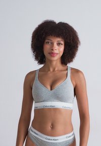 Grå sømløs bralette med justerbare stropper og en hvit Calvin Klein logo-bånd. Matchende grå bikini-truse har det samme logo-båndet.