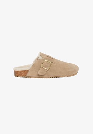 Beige suède pantoffel met een nepbont voering, kurken middenzool en een gouden metalen gespaccent. Laag profiel ontwerp met een getextureerde zool.