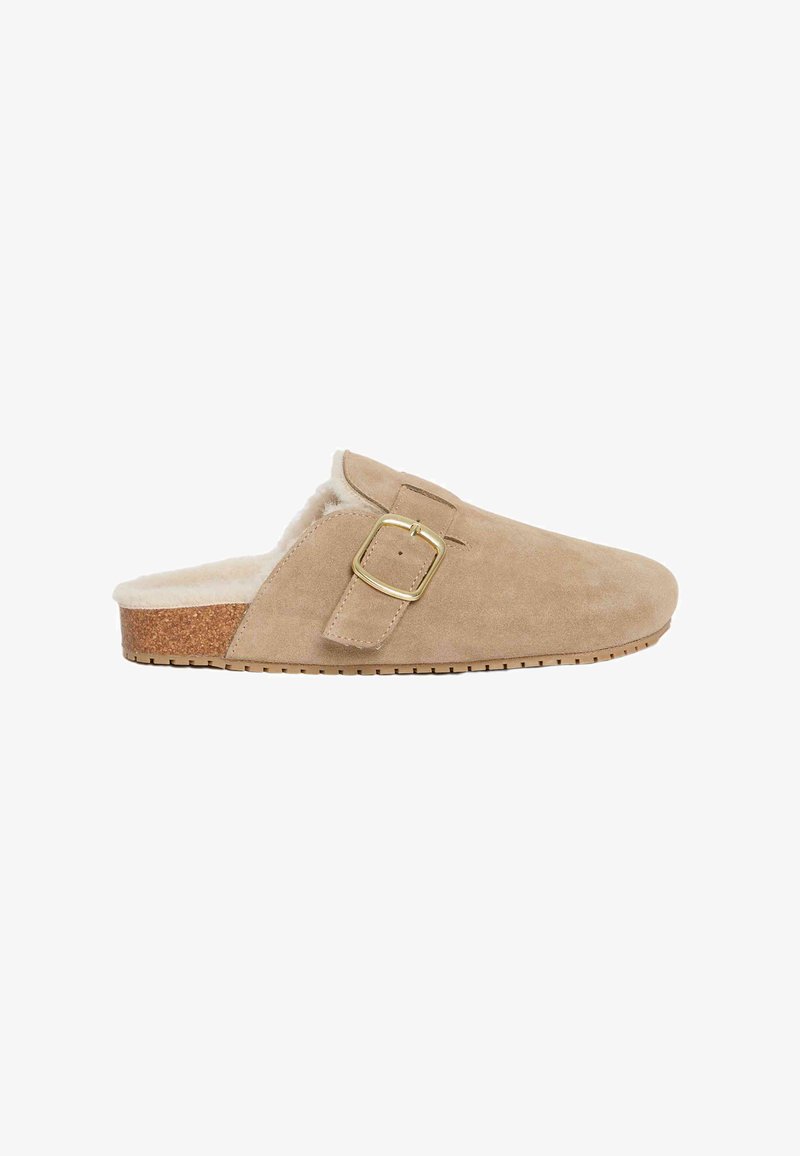 Beige mockasiner i mockasammet med fuskpälsfoder, korkmittsula och en detalj av gyllene metallspänne. Låg profil med en texturerad sula.