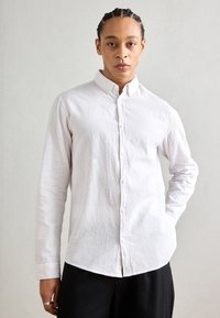 Camisa blanca de botones, hecha de un tejido texturizado, con cuello, mangas largas y dobladillo redondeado; combinada con pantalones negros.