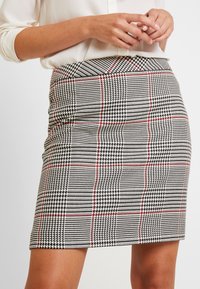 Zwart-wit houndstooth rok met rode accentlijnen, strak ontwerp, kniehoogte, met een gladde textuur en gestructureerde vorm.