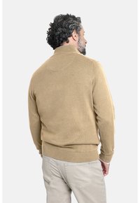 Suéter de punto beige con cuello de media cremallera, puños y dobladillo acanalados, que presenta una textura suave y un corte casual. Llevado con pantalones de color claro.
