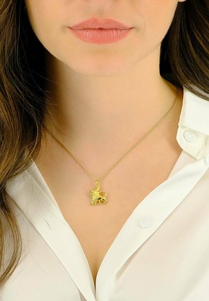 Collier pendentif en or avec un design détaillé de licorne, suspendu à une fine chaîne, porté sur une chemise blanche à col.