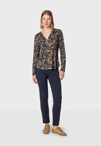 Navy long-sleeve top with gold floral pattern, v-neckline, paired with navy slim-fit trousers and tan shoes. Smooth fabric texture.