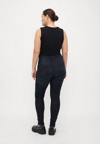 Černý top bez rukávů s kulatým výstřihem, spárovaný s tmavě modrými skinny džíny a černými platformovými botami se stříbrnými nýty.