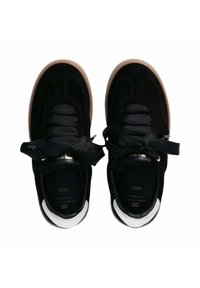 Sneakers in suede nero con spesse stringhe nere, punta arrotondata e suola in gomma color caramello. Presentano dettagli metallici vicino al tallone.