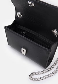 Sac à main en cuir noir texturé avec quincaillerie argentée, doté d'une bandoulière en chaîne, d'une fermeture magnétique et de plusieurs compartiments à l'intérieur.