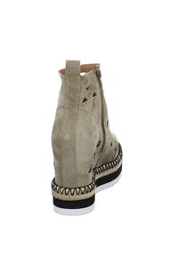 Botín con tacón cuña de ante beige, con detalle de corte, cierre de cremallera y acento de yute trenzado en la suela, presentando una base blanca y negra.