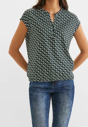 Kurzärmlige grün-weiße Bluse mit Muster, einer eingeschnittenen Kragen und Raffung in der Taille, kombiniert mit blauen Jeans.