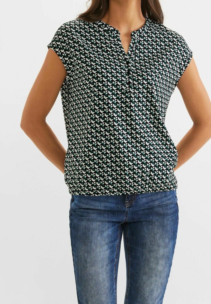 Krátký rukáv, zelená a bílá vzorovaná blůza s výstřihem a nařasením v pase, doplněná modrými džíny.