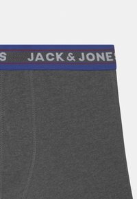 Grå bomullsbokser med en bred blå og svart elastikk med "JACK & JONES"-logo i hvitt, glatt tekstur og tettsittende design.