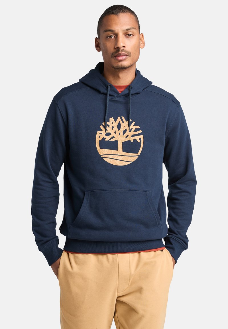 Granatowy hoodie wykonany z miękkiego materiału, z dużym beżowym logo drzewa, kieszenią z przodu i kapturem ze sznurkiem. Wykończony ściągaczami przy mankietach.