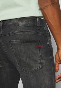 Jeans de mezclilla gris oscuro con un parche de cintura de cuero negro con logotipo embosado, detalle de costura roja en el bolsillo trasero y diseño de bolsillo clásico.
