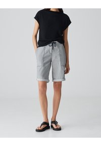Black short-sleeve top, gray striped bermuda shorts with rolled cuffs, drawstring waist, and flat black sandals with buckle detail.