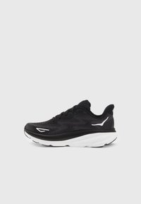 Scarpa sportiva nera con tomaia in mesh, accenti bianchi, intersuola morbida, punta rotonda e design con lacci. Superficie texturizzata con schemi diagonali.