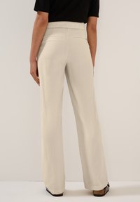 Wide-leg trousers in light cream fabric with a textured finish. Elastic waistband and two back pockets, paired with black block-heeled shoes.