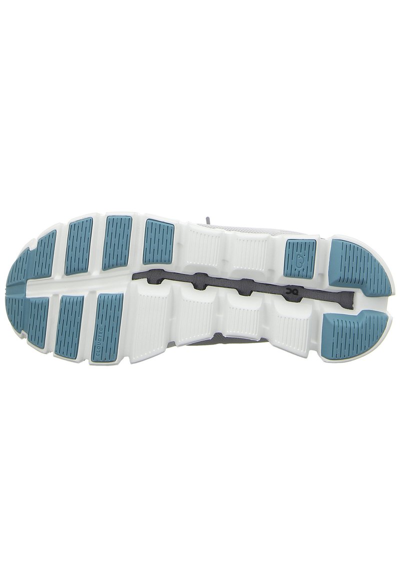 Suela flexible de zapatilla de running blanca con almohadillas de tracción azules y líneas de surcos negras para amortiguación y agarre.