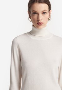 Weißer Rollkragenpullover aus weichem Stoff mit langen Ärmeln. Hat eine figurbetonte Silhouette und eine glatte Textur. Schlichtes Design ohne Muster.