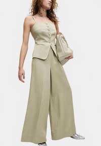 Jasnozielony dwuczęściowy strój składający się z dopasowanego, zapinanego na guziki topu oraz spodni o szerokich nogawkach. Do tego teksturowana torebka i metaliczne buty.