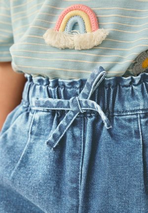 Modrá pruhovaná košile s duhovou nášivkou; lehké džíny šortky s elastickým pasem a mašlí uvázanou vpředu.