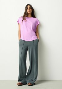 Rosa T-Shirt mit kurzen Ärmeln und rundem Ausschnitt, kombiniert mit weiten grauen Hosen mit Seitennähten und weicher Textur.