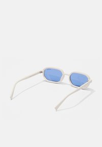 Stijlvolle zonnebril met een off-white plastic montuur, octagonale vorm en blauwe lenzen; slanke pootjes taperen naar de uiteinden.