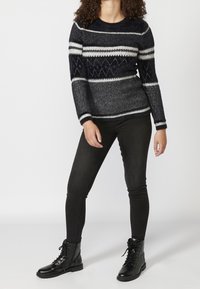 Marinblå tröja med geometriska mönster och vita ränder, kombinerad med svarta skinny jeans och svarta snörstövlar. Mjuk textur, rund halsringning.