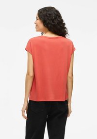 Top corto de color coral con un ajuste holgado, textura suave, escote redondo y aberturas laterales, combinado con pantalones negros de pierna ancha.