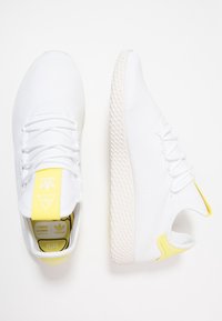 Vita nät sneakers med texturerad ovandel, gula accenter på hälen och en gummisula med ett distinkt mönster.